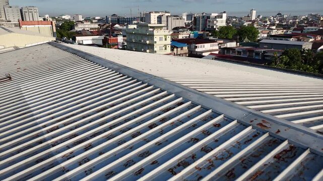 A view from the top of a corrugated metal roof with rusted panels and industrial-style urban buildings.