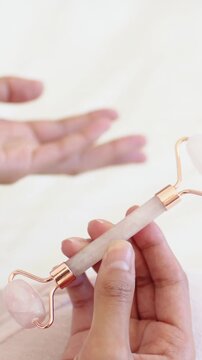 Vertical video: Bringing hand holding rose quartz roller into view on bed showing scale, copy space