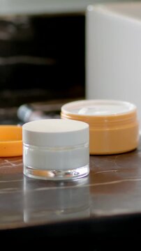 Vertical video: Staying centered white jar on vanity, camera shifting to show orange cream and tube