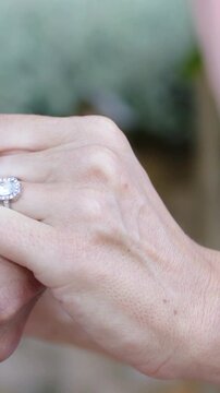 Vertical video: Entering right hand adjusting halo diamond ring on left hand in garden, pink sleeve