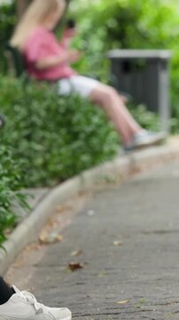 Vertical video: Scrolling blonde teen in pink top using phone on path while bicycle enters, passing