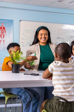 Indian woman teacher with African American children spraying fern at school table with spray bottle