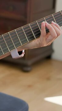 Vertical video: Recording as camera focusing, left hand practicing chords on guitar in bedroom