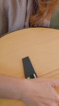Vertical video: Strumming woman in beige top playing at home, hand touching acoustic guitar strings