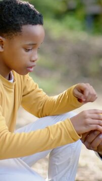 Vertical video: Reaching child in mustard top studying yellow object in park, adult hand offering