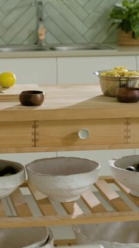 Vertical video: Panning camera revealing light-wood island with bowls, colander, lemon, backsplash