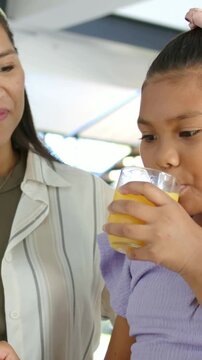 Vertical video: Guiding woman pointing pencil at tablet, girl sipping juice at table, copy space