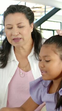 Vertical video: Holding cup, leaning mother in shirt guiding daughter talking at home with juice