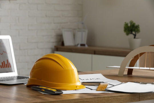 Yellow hard hat, laptop with charts, and architectural blueprints on wooden desk for construction planning