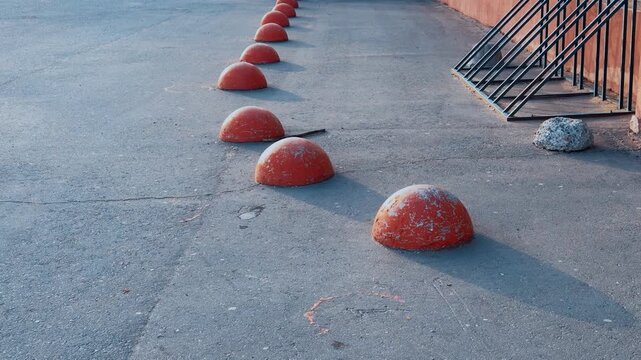 Red hemispheres lining empty pedestrian lane, bicycle rack against building wall, sunlit asphalt textures and long shadows, quiet