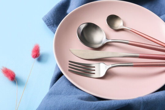 Table setting with silver cutlery, plate, napkin and dried lagurus on blue background