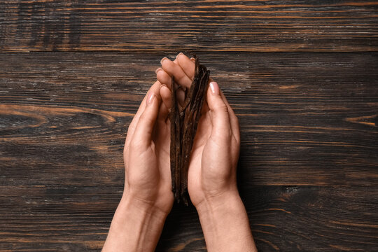 Female hands holding aromatic vanilla sticks on wooden background
