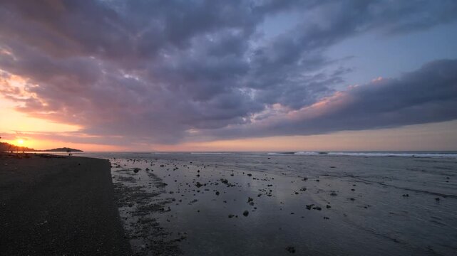 Dramatic sunset over Pemuteran Beach, Bali, with dark storm clouds gathering above calm coastal waters and a volcanic shoreline, creating a striking tropical seascape at dusk
