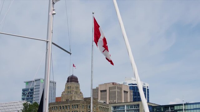 The flag of Canada moves in the wind in downtown Halifax. The buildings stand tall against the sky. People pass by enjoying the day in the city of Halifax, Nova Scotia
