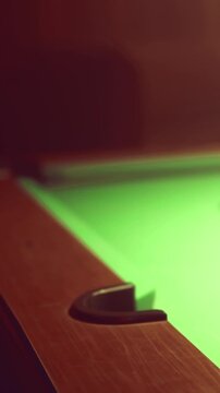 A pool table is shown with a green surface. The edge of the table is in focus while a ball sits nearby, suggesting an active game. The setting captures the atmosphere of a billiards venue.