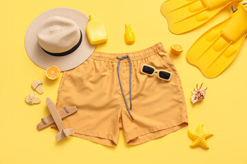 Summer vacation travel essentials flat lay with swim trunks, sunscreen, hat, and flippers on yellow background © Pixel-Shot
