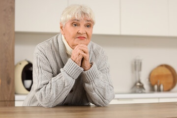 Fototapeta premium Beautiful thoughtful senior woman near table in kitchen at home