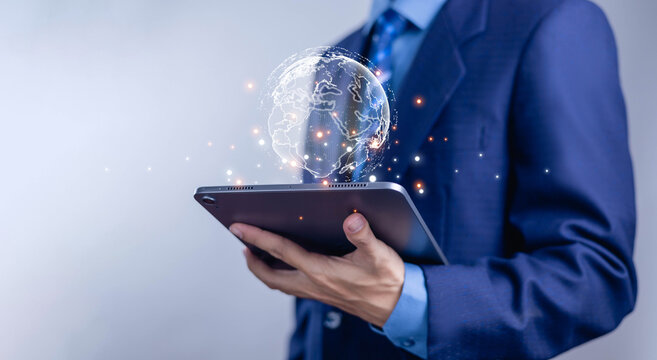 Business technology and global digital network concept with a businessman holding a tablet and holographic world globe, representing digital transformation, cloud computing.
