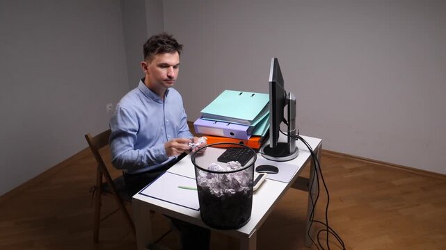Frustrated worker throwing crumpled paper into a crowded wastebasket on a white office desk with a computer monitor and binders, symbolizing stress, failure, and creative block in a workspace