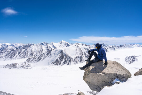 Mountain Climber Sitting on Summit Rock Overlooking Vast Glacial Panorama of Tsambagarav Range, Mongolian Altai