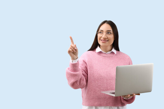 Beautiful young female programmer with laptop pointing at something on blue background