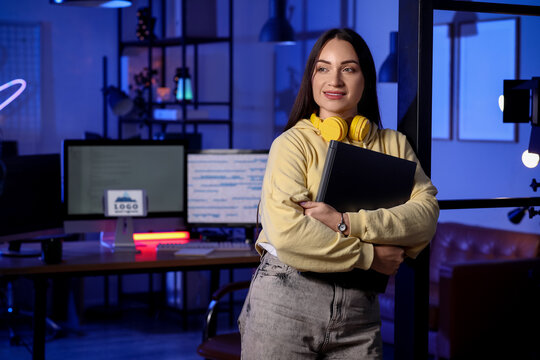 Beautiful young female programmer with laptop in modern office at night