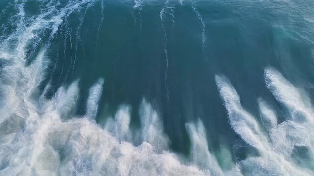 A mesmerizing drone shot looking directly down at a massive emerald green ocean wave curling and breaking into rich white sea foam.