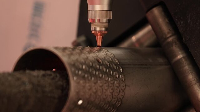 Industrial laser cutting machine precisely engraves intricate pattern onto metal pipe with sparks flying.