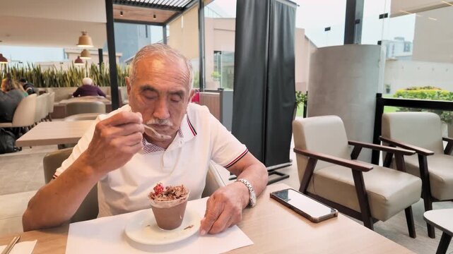 Active senior man enjoying a chocolate mousse dessert while dining at a modern cafe. Authentic retirement lifestyle, independence, wellbeing and quality of life during the golden years.