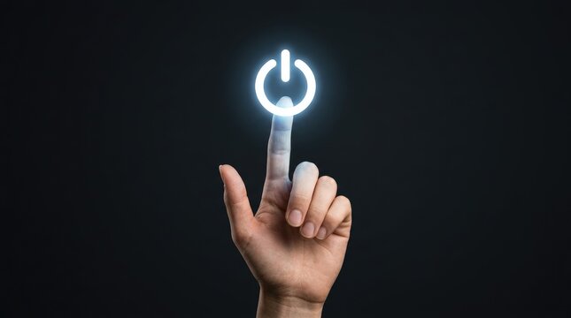 Human index finger pressing a glowing white power button icon floating in the air against a dark grey studio background