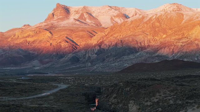 Volcanic canyon and mountain range glowing at sunrise in La Payunia, aerial telephoto pan right