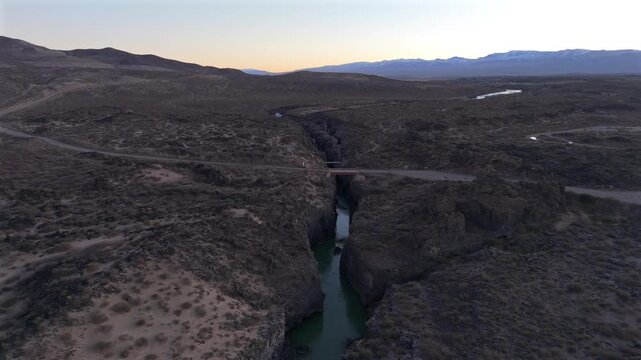 Volcanic canyon in La Payunia Provincial Reserve, Malarg&uuml;e, Mendoza, Argentina, carved through basaltic terrain with a bridge crossing above a confined river channel, drone pullback shot.