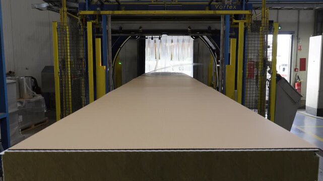 Camera rises from raw rock wool texture to reveal a white sandwich panel advancing into an automated orbital wrapping machine.