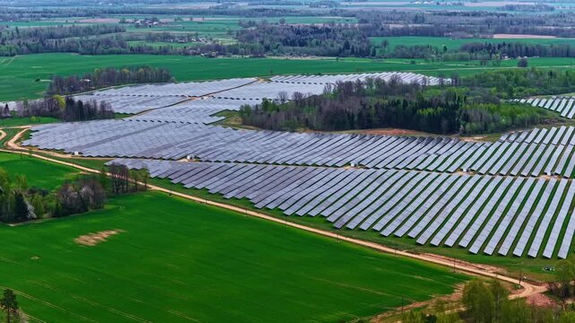 Sweeping solar installation flanked by vivid green crop fields and gravel access roads. Latvia, Latvija.