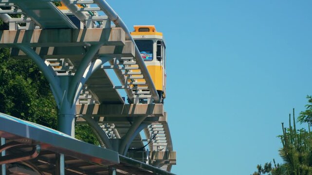 Low angle tracking of yellow Sky Capsule retro cars moving on elevated arched track structure against blue sky at Haeundae Blue Line Park in Busan Korea