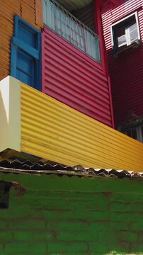 POV walking colorful corrugated metal facades in yellow, red, green and blue with tile rooftop detail in Caminito, La Boca, Buenos Aires, Argentina.