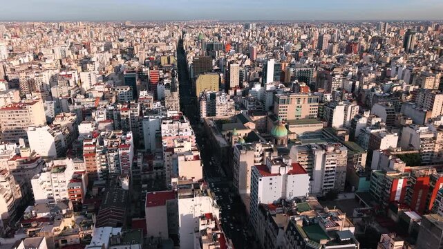 Major avenue cuts through the dense urban fabric of Buenos Aires, Argentina, lined with residential towers, commercial buildings and continuous city blocks, slow orbit drone shot.