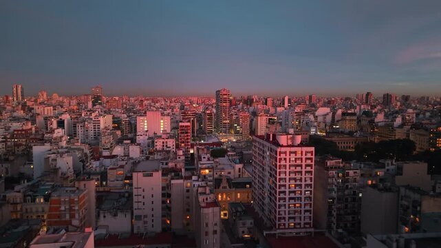 Residential towers and commercial buildings glow under sunset light across Buenos Aires, Argentina, revealing dense urban fabric and metropolitan skyline, drone forward flyover shot.
