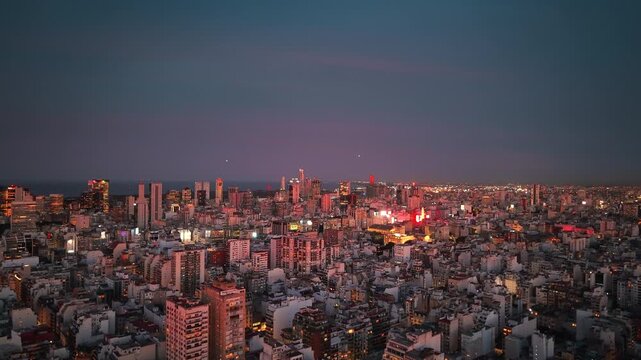 Barrio Norte and central Buenos Aires glow with evening lights as residential towers and commercial buildings extend across the Argentine capital, drone ascent shot, Rio de la Plata in the background