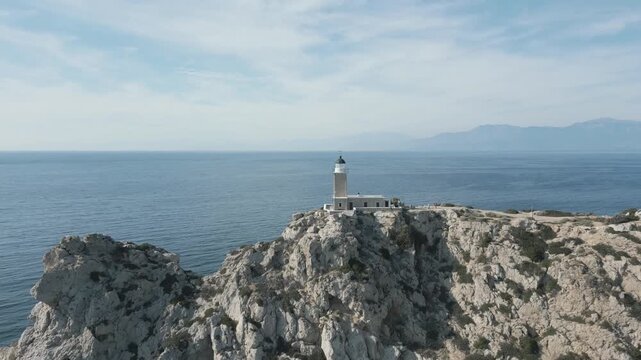 Stunning drone video rises above Cape Prasonisi Lighthouse perched on rugged cliffs, surrounded by deep blue Aegean Sea, under crisp daylight with panoramic coastal scenery.