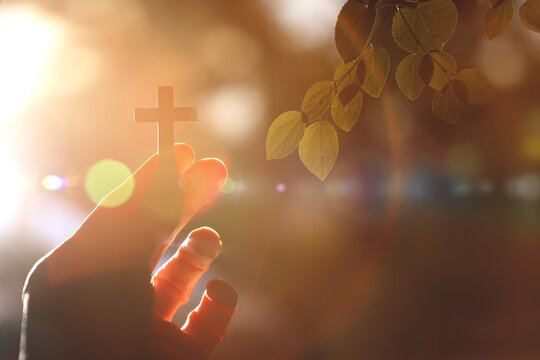 Brightly shining sunlight and a Christian holding the cross of salvation of Jesus Christ in their hands, Christian faith background
