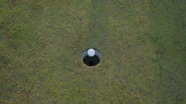 Spinning shot of golf ball being holed at sunset