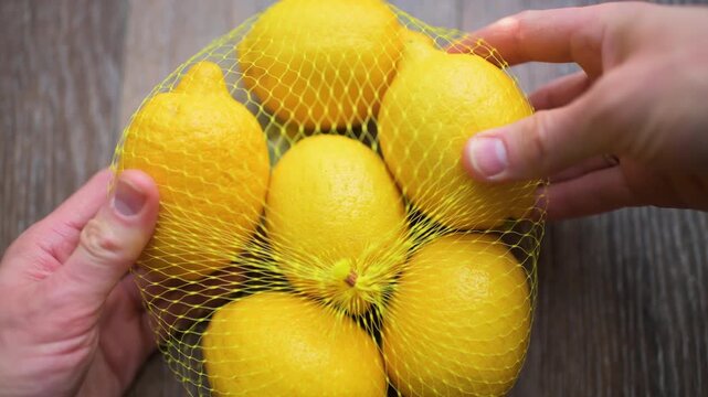 Lemon lemons bundle in mesh bag from grocery store supermarket hand holding macro closeup on kitchen wooden table
