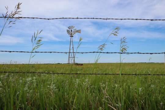 Historic Prairie Windmill Viewed Through Barbed Wire Fence in Kansas Grassland