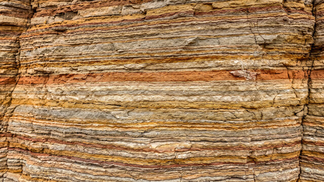 tight close up of layered limestone rock strata revealing a complex linear geological timeline with earthy terracotta and beige color transitions