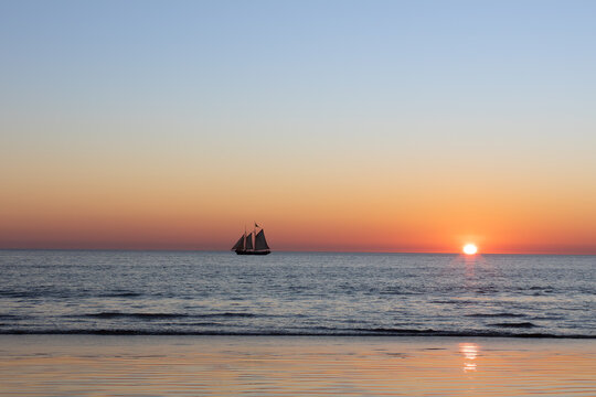 Sun setting over the Indian Ocean with an old pearling lugger sailing off  Cable Beach, Broome.