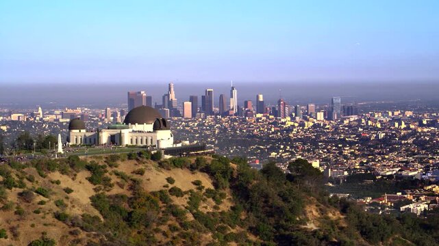 Cinematic compressed aerial shot of Griffith Observatory on Mount Hollywood with DTLA skyscrapers in the background.