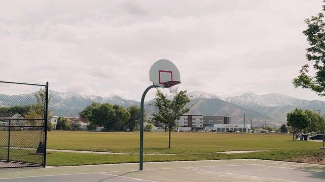 Steady glide follow shot tracking basketball hoop with open park and mountain range in the background.