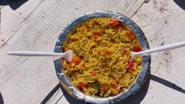 spicy vegetable maggi noodles served in disposable bowl at outdoor food stall