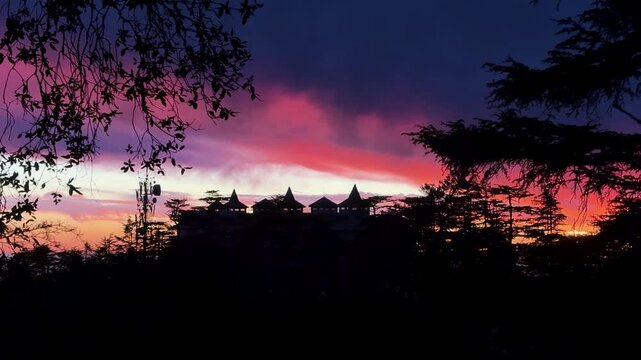 silhouette of historic building and pine trees against dramatic sunset cloudscape